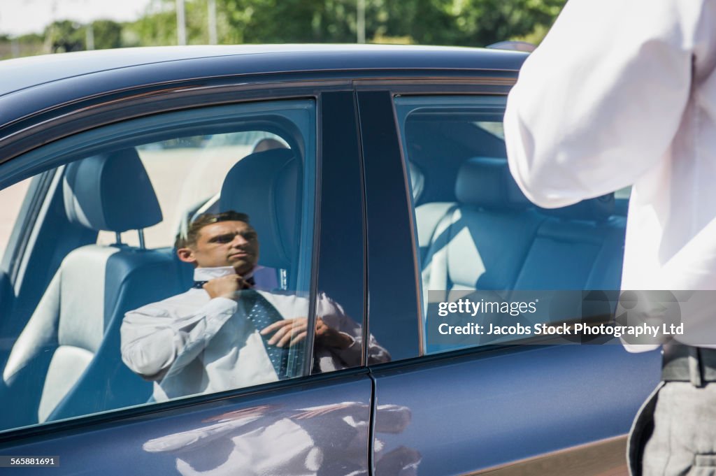 Caucasian businessman adjusting tie in car window