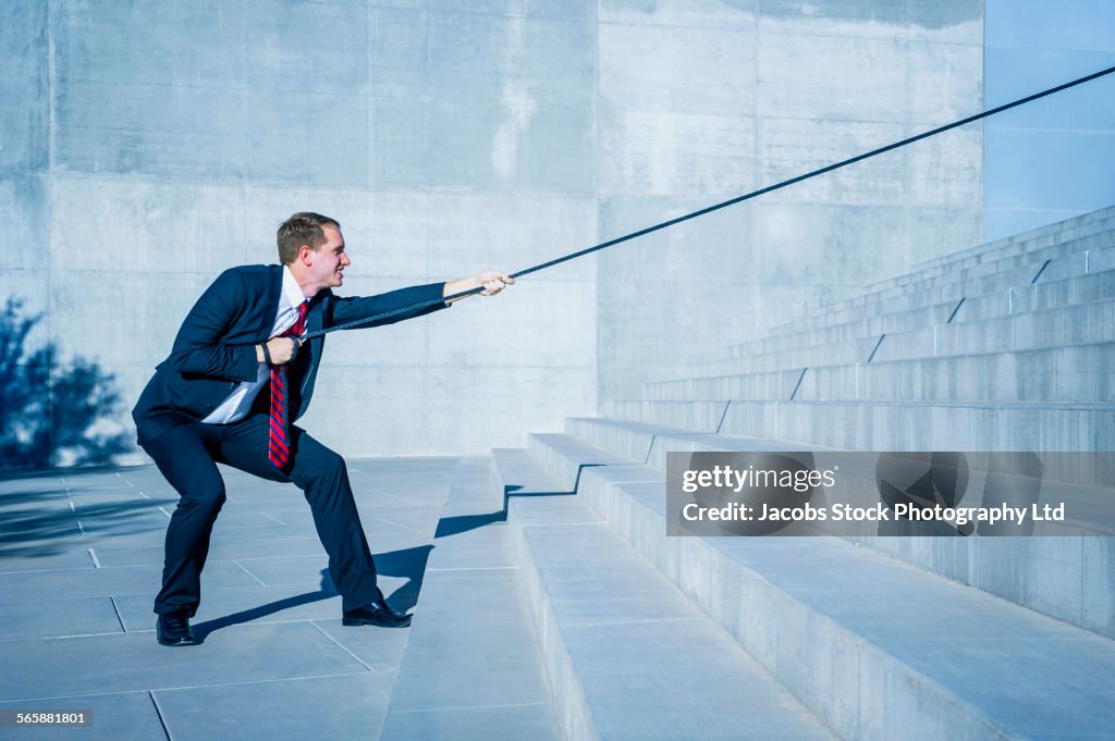 Caucasian businessman pulling rope down outdoor staircase