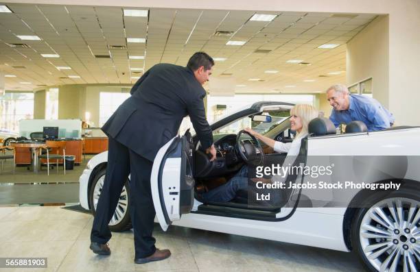 salesman showing convertible to couple in car dealership - sports car showroom stock pictures, royalty-free photos & images