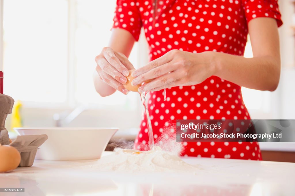 Mixed race woman cracking egg in kitchen