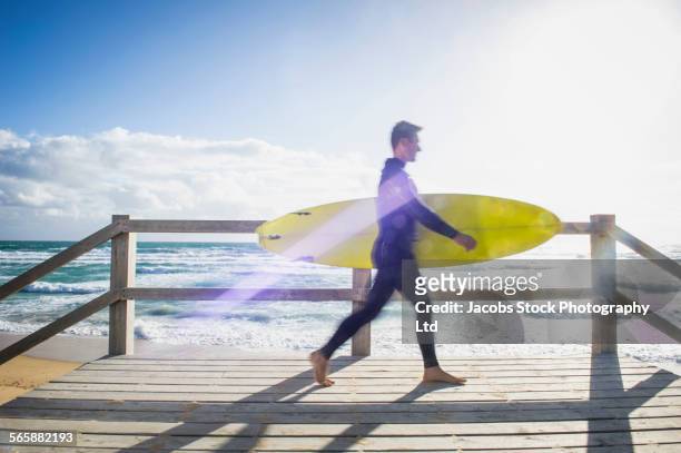 caucasian surfer carrying surfboard on beach boardwalk - melbourne stock pictures, royalty-free photos & images