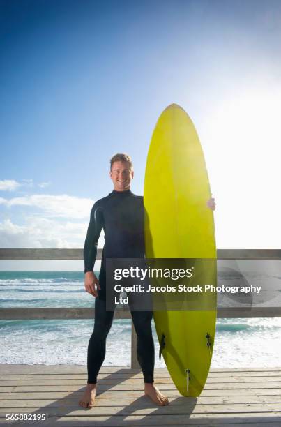 caucasian surfer holding surfboard on beach boardwalk - surfer wetsuit stockfoto's en -beelden