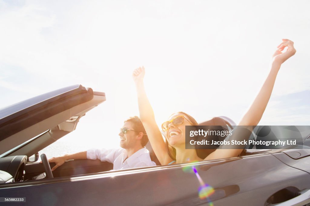 Couple driving in convertible under sunny sky