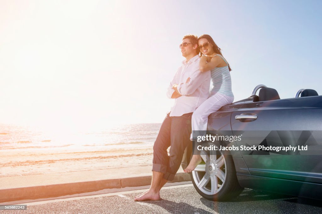 Couple relaxing near convertible in beach parking lot