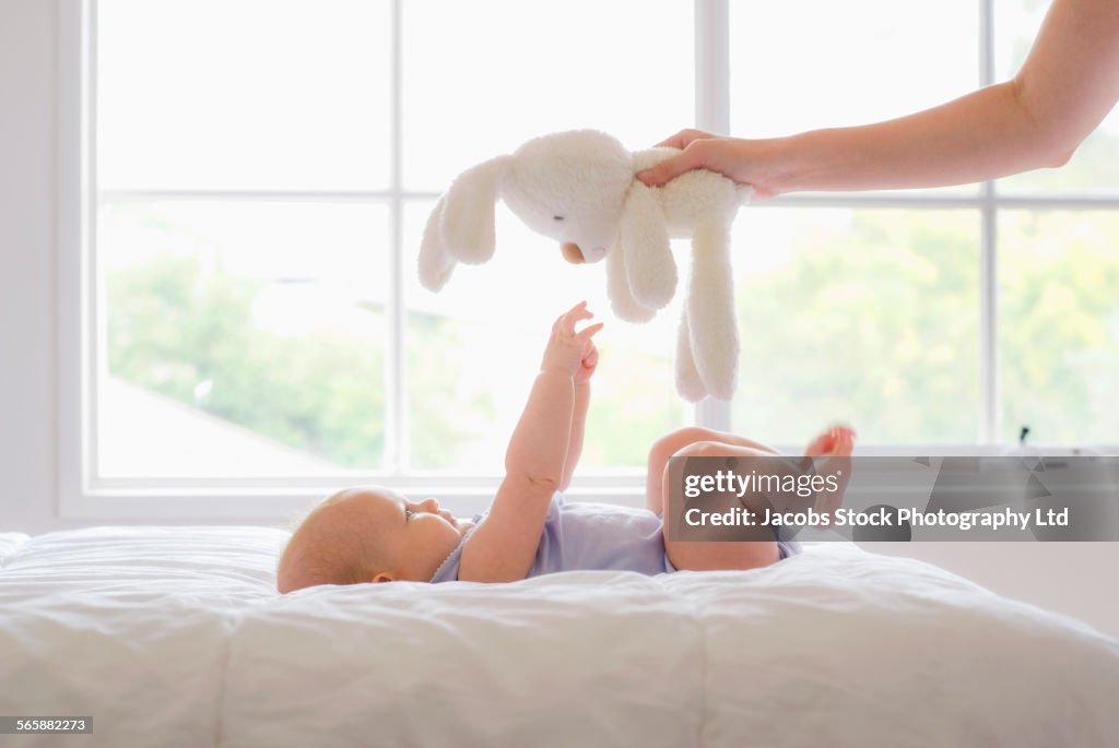 Caucasian mother and baby playing with stuffed animal in bedroom