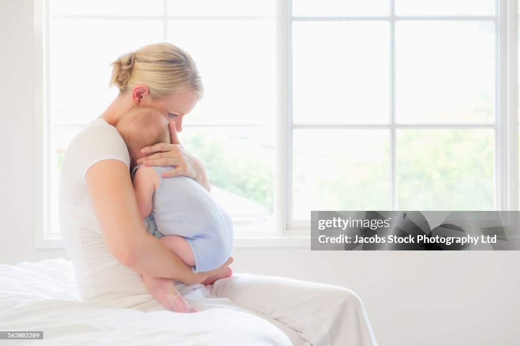 Caucasian mother cuddling baby on bed