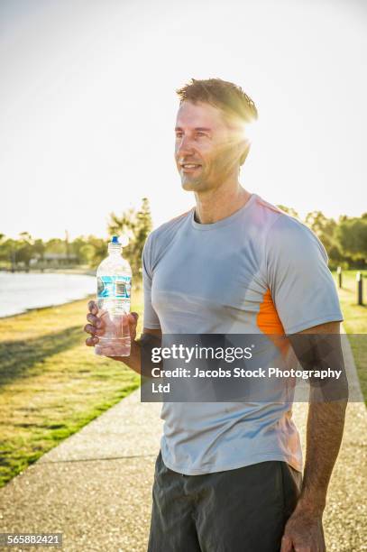 sweaty caucasian runner drinking water bottle in park - mann wasser trinken sport stock-fotos und bilder