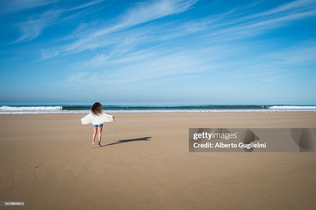 Caucasian woman walking on beach under blue sky