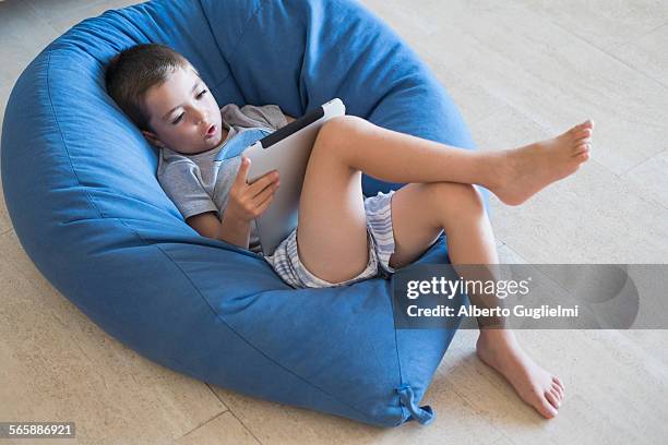 caucasian boy using digital tablet in beanbag chair - beanbag chair stockfoto's en -beelden