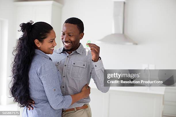 couple hugging and holding keys in new home - home ownership keys stock pictures, royalty-free photos & images