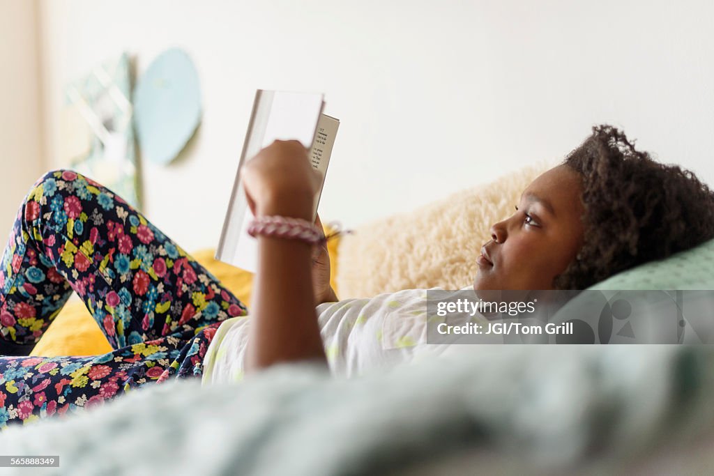 Black girl reading book on bed