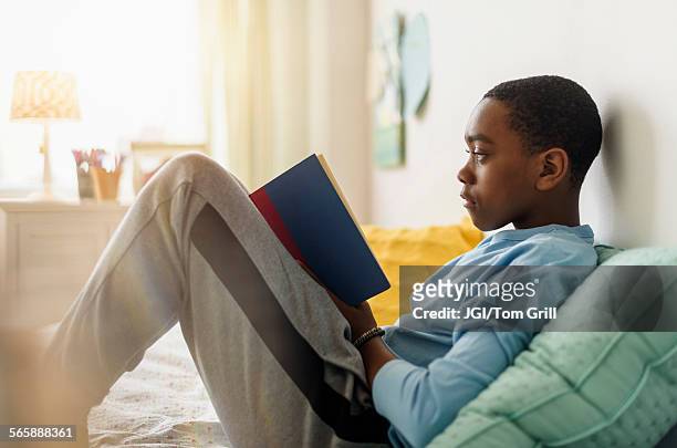 black boy reading book on bed - boy sitting on bed stock-fotos und bilder