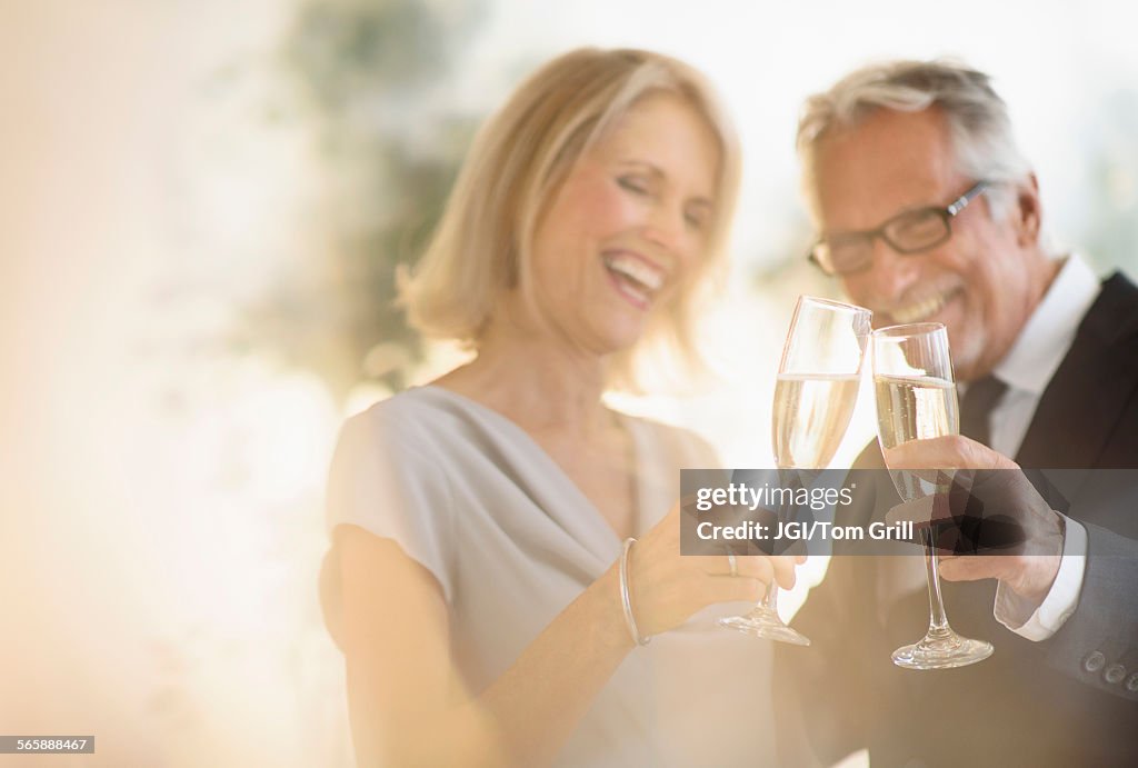 Smiling older Caucasian couple toasting with champagne