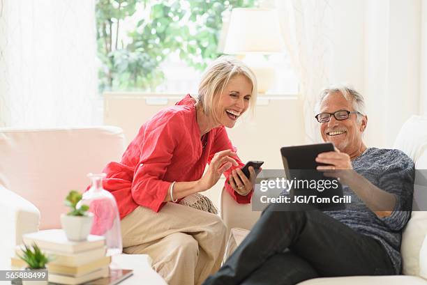 older caucasian couple using technology in living room - couple de vieux drole photos et images de collection