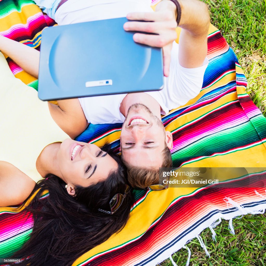 Hispanic couple taking selfie on blanket in park