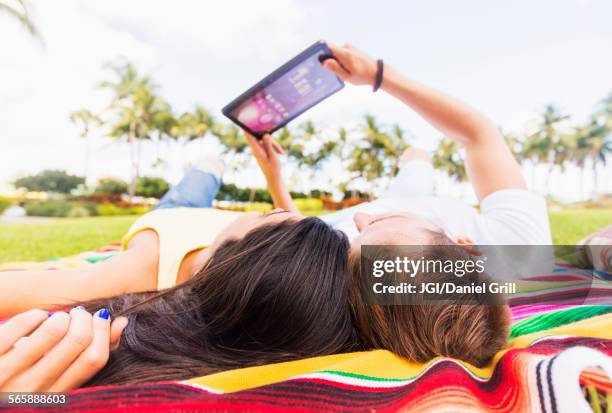 hispanic couple using digital tablet on blanket in park - tablet paar sommer stock-fotos und bilder