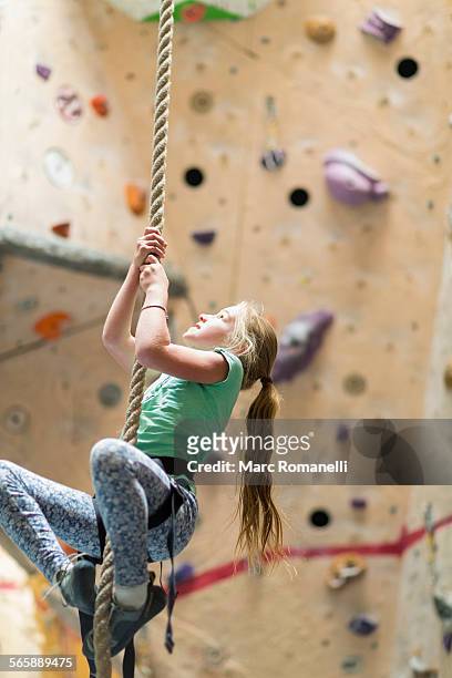 Caucasian girl climbing rope on rock wall indoors