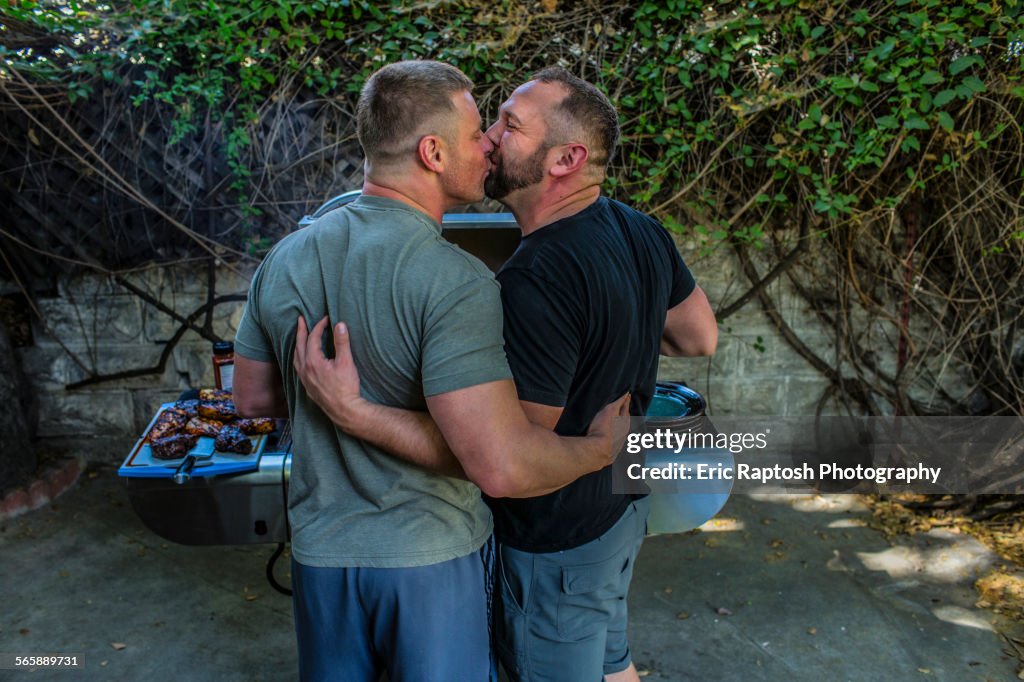 Gay couple kissing and grilling food in backyard