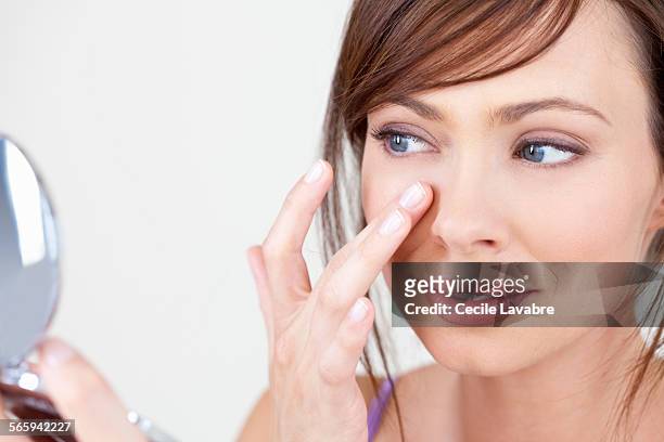 woman examining face in her mirror - makeup face stock-fotos und bilder