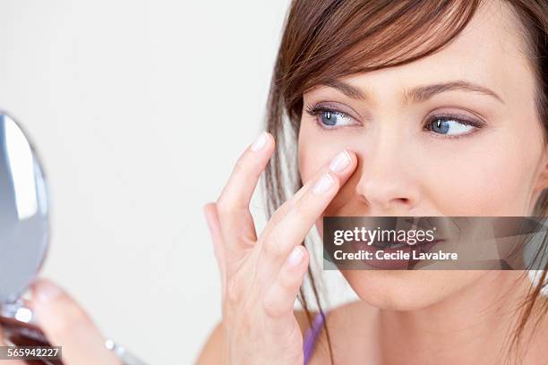 woman examining face in her mirror - femme make up mauve photos et images de collection