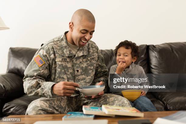 mixed race soldier father and son from bowls on sofa - military bowl stock pictures, royalty-free photos & images