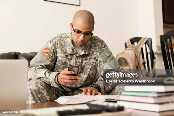 mixed race soldier texting on cell phone and studying on sofa - military training stock pictures, royalty-free photos & images
