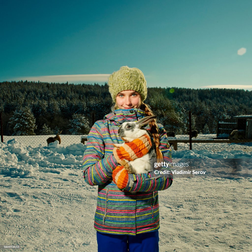 Caucasian girl hugging rabbit in snowy field