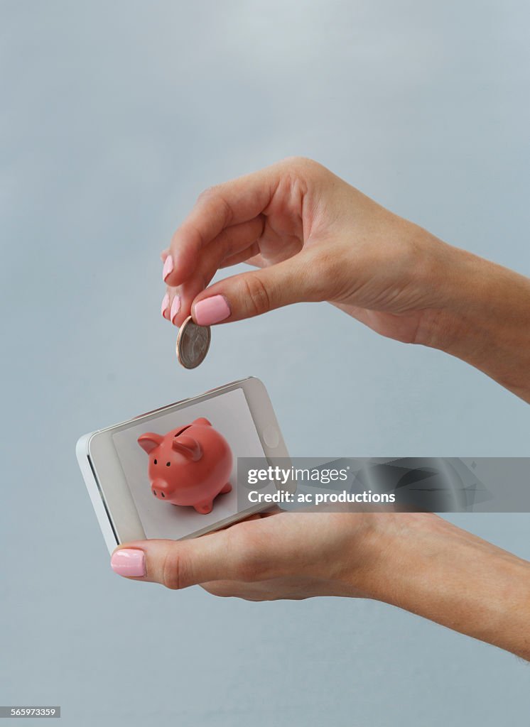 Caucasian woman depositing coin in cell phone piggy bank