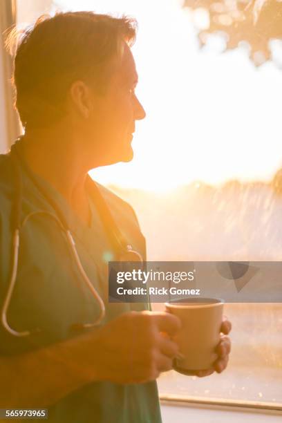 caucasian nurse drinking cup of coffee at window - nurse thinking stock pictures, royalty-free photos & images