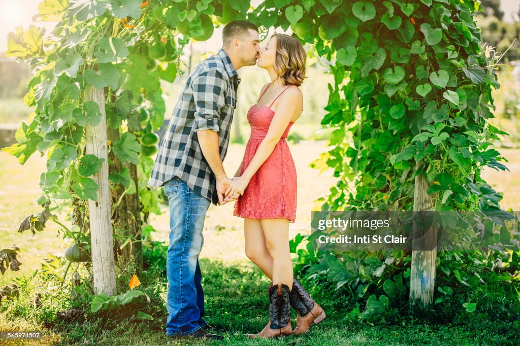 Caucasian couple kissing under leafy arch