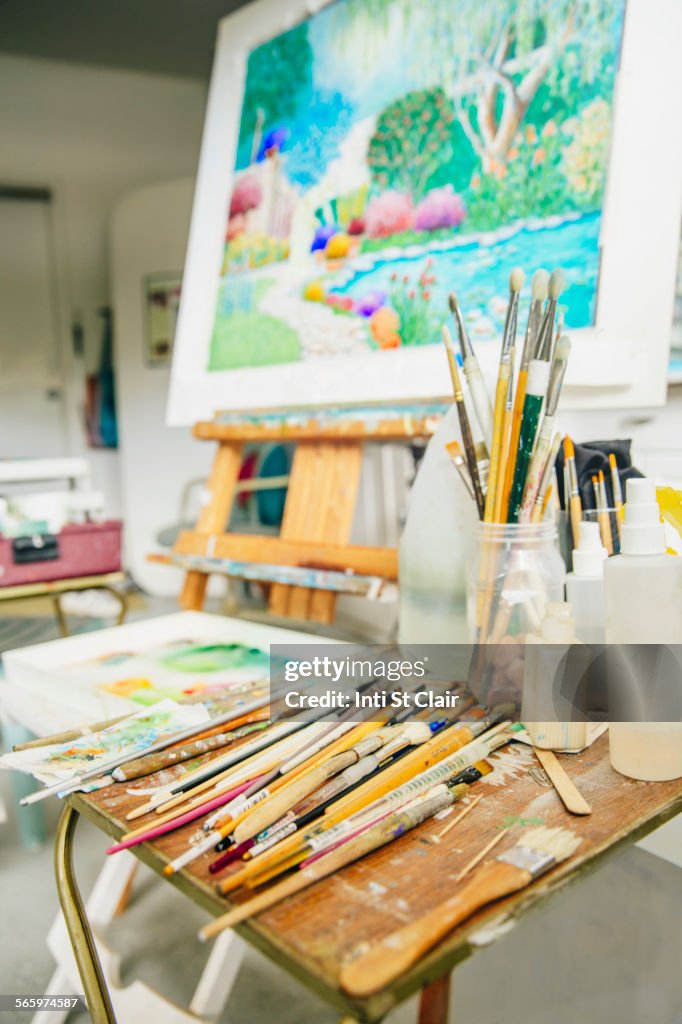 Paintbrushes, palette and easel with painting in studio