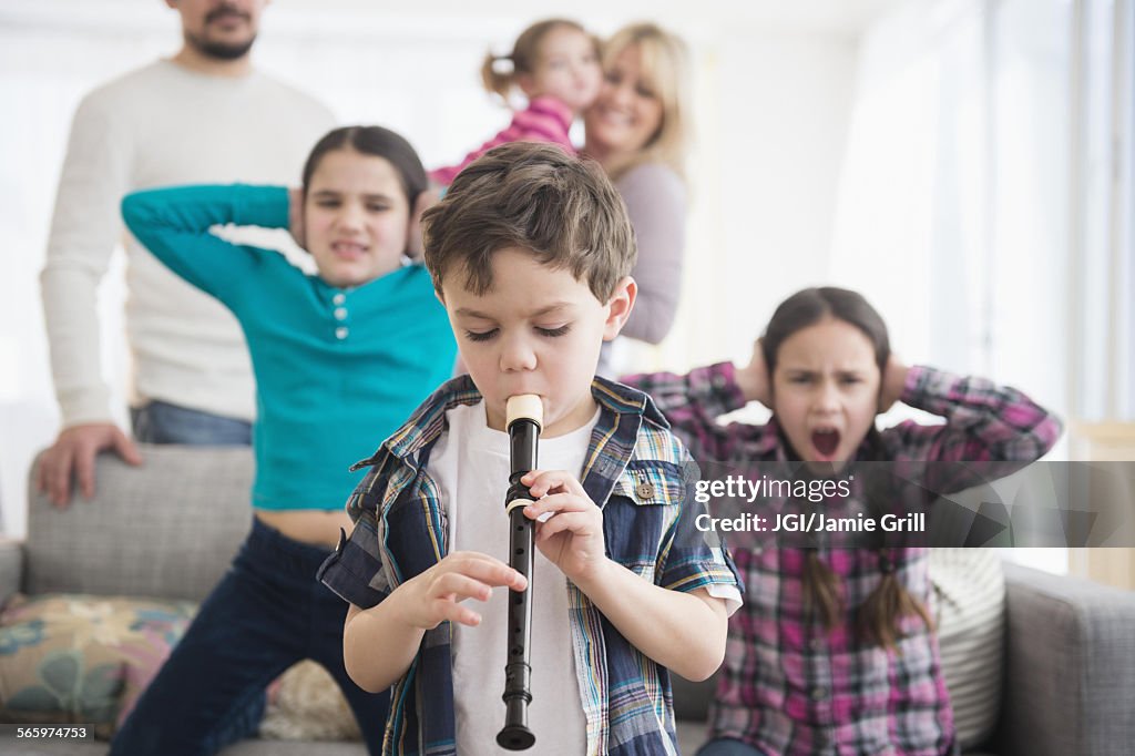 Caucasian family covering ears with boy playing recorder