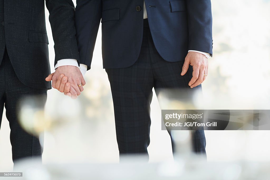 Caucasian gay grooms holding hands at wedding