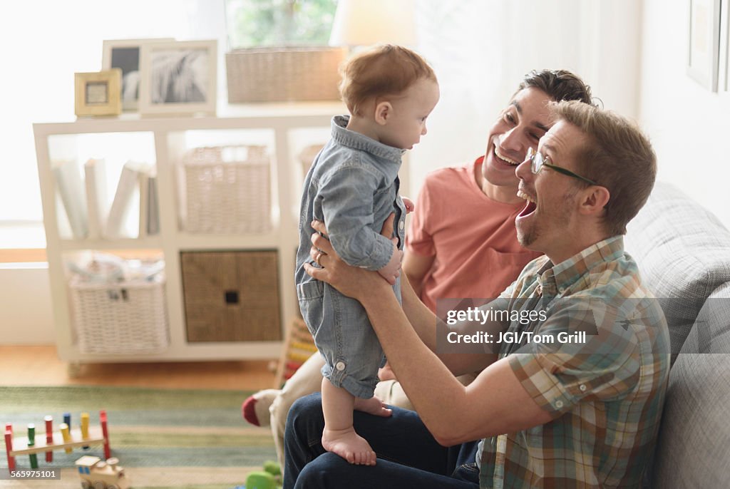 Caucasian gay fathers and baby playing in living room