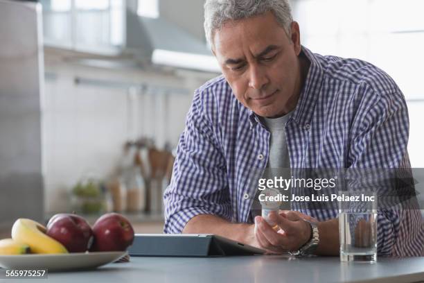 hispanic man examining prescription bottle in kitchen - prescription medicine stock pictures, royalty-free photos & images