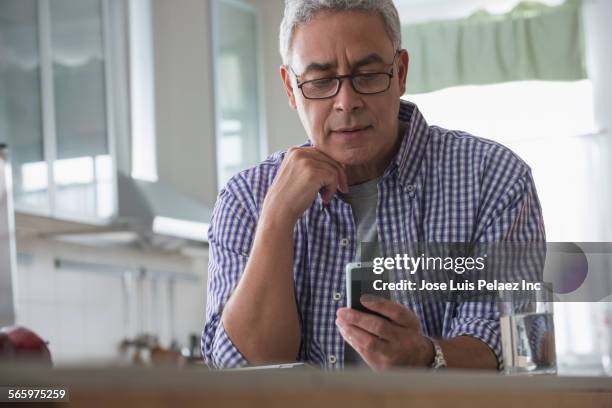 hispanic man using cell phone in kitchen - receiving text stock pictures, royalty-free photos & images