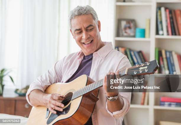 hispanic man playing guitar in living room - alleen seniore mannen stockfoto's en -beelden