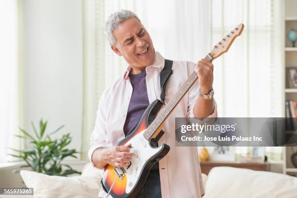 hispanic man playing electric guitar in living room - playing electric guitar stock-fotos und bilder