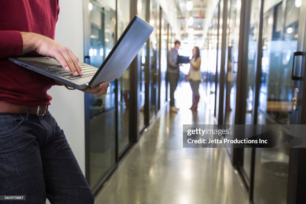 Businessman using laptop in office hallway