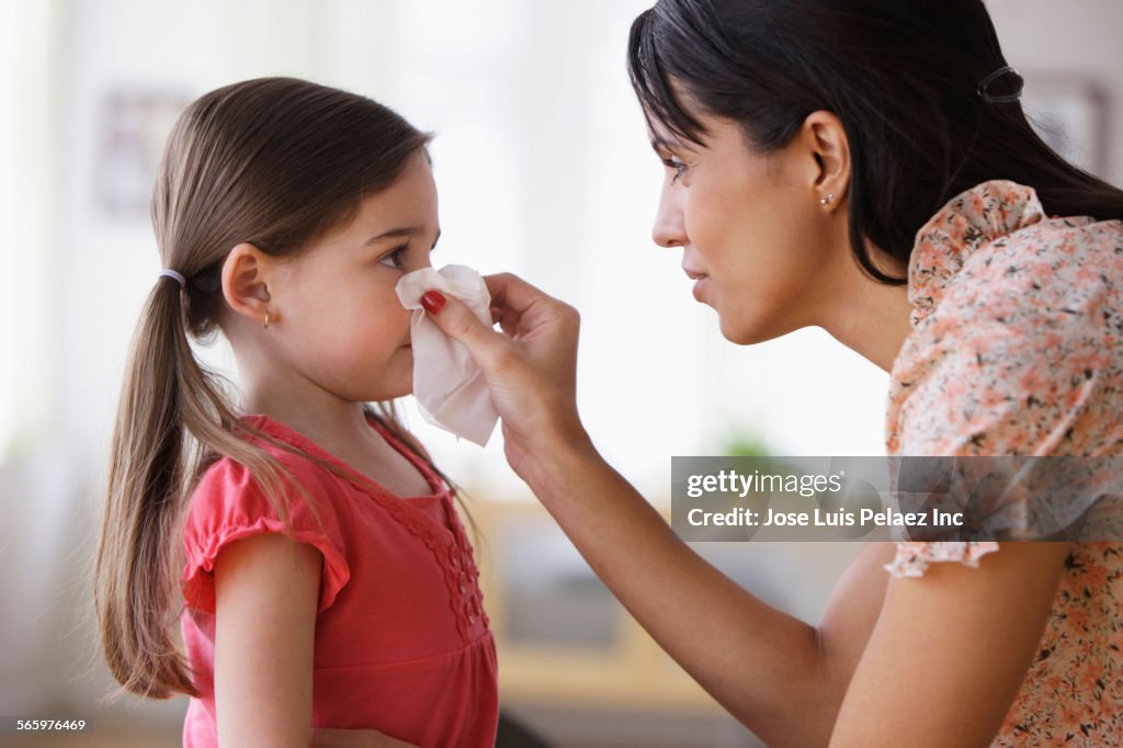 Mother wiping nose of daughter with tissue