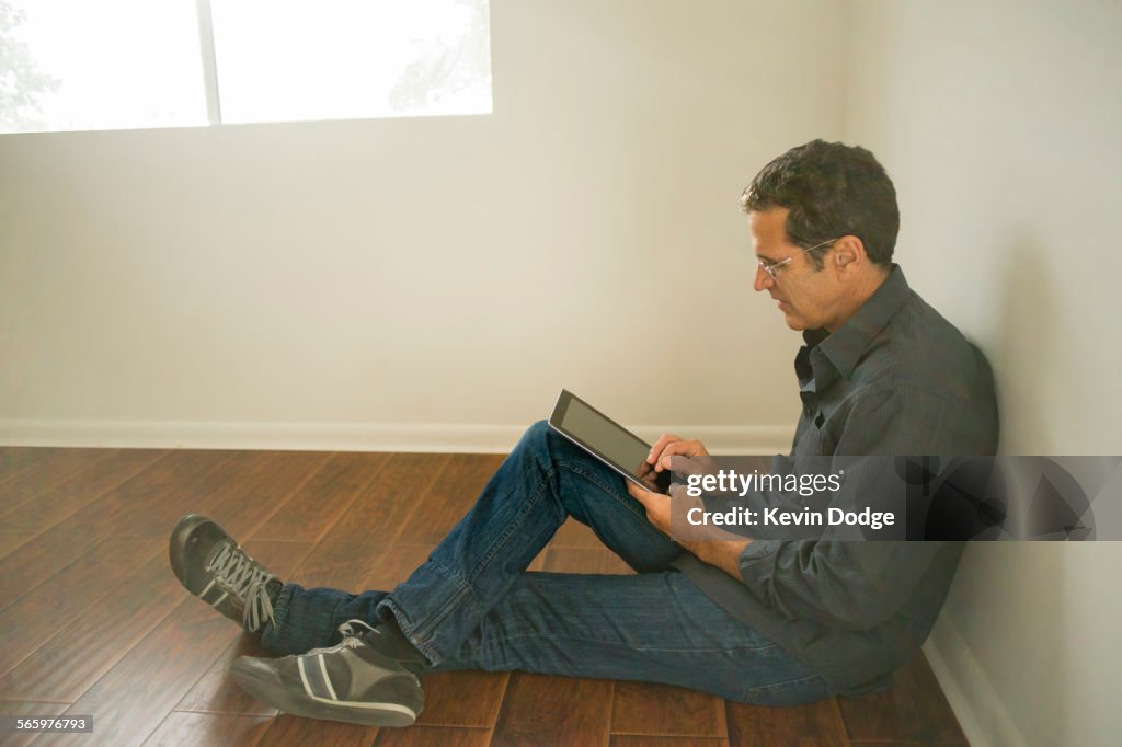 Hispanic man using digital tablet on floor of empty room