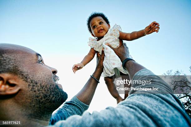 black father holding baby daughter under blue sky - black baby foto e immagini stock