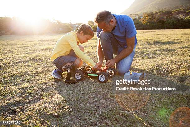 caucasian father and son playing with remote control cars in field - remote control car games stockfoto's en -beelden