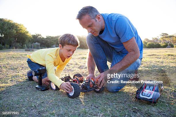 caucasian father and son playing with remote control cars in field - toy cars photos et images de collection
