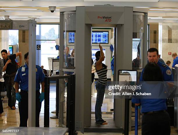 Travelers pass through security, including a new body scanner, shown at right, atJohn Wayne Airport's new Terminal C. Five new security screening...