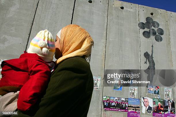 Palestinian woman carries her child past grafitti, by the British artist Banksy, on Israel's separation wall January 16, 2006 near the Israeli army's...