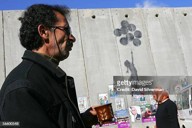 Palestinian taxi driver drinks his coffee as he waits for passengers alongside grafitti, by the British artist Banksy, on Israel's separation wall...