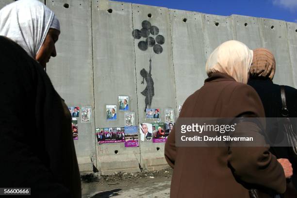 Palestinian women pass grafitti by the British artist Banksy on Israel's separation wall January 16, 2006 near the Israeli army's Qalandia checkpoint...