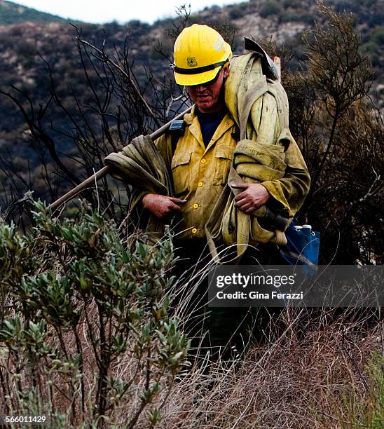 Strike team member from the Angeles National Forest carries hoses and his hot spot tools through the rugged terrain while mopping up the Gorgonio...