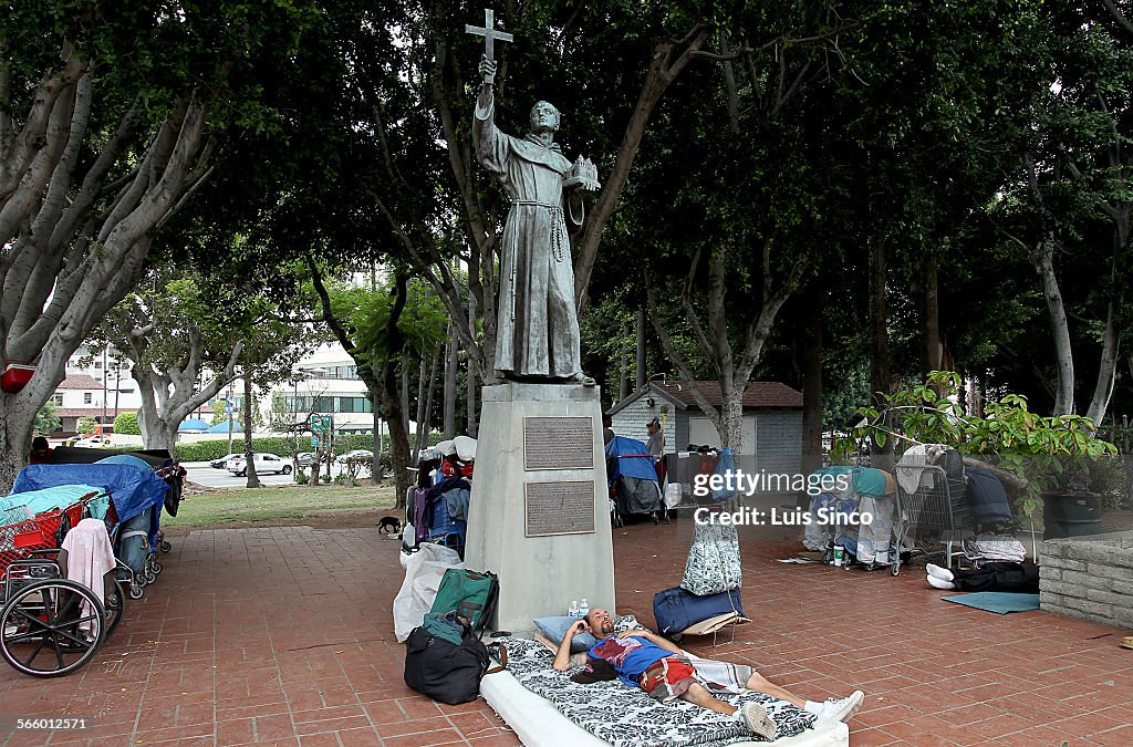 A homeless man sleeps beneath a statue of Father Junipero Serra at Serra Park in Los Angeles on Thu